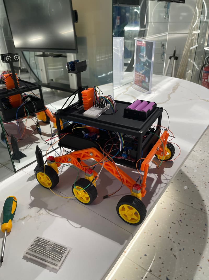 The first Parakh prototype with its electronics exposed: breadboard and purple 18650 battery pack on the deck, orange truss suspension arms, yellow wheels.