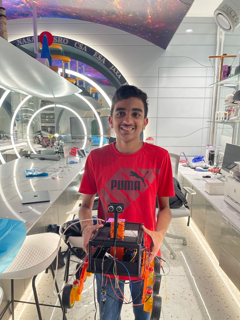 Aarav Goyal in the makerspace, smiling and holding the Parakh rover up to the camera.